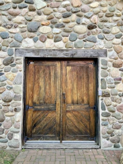 A rustic wooden door with iron hinges set in a stone wall.