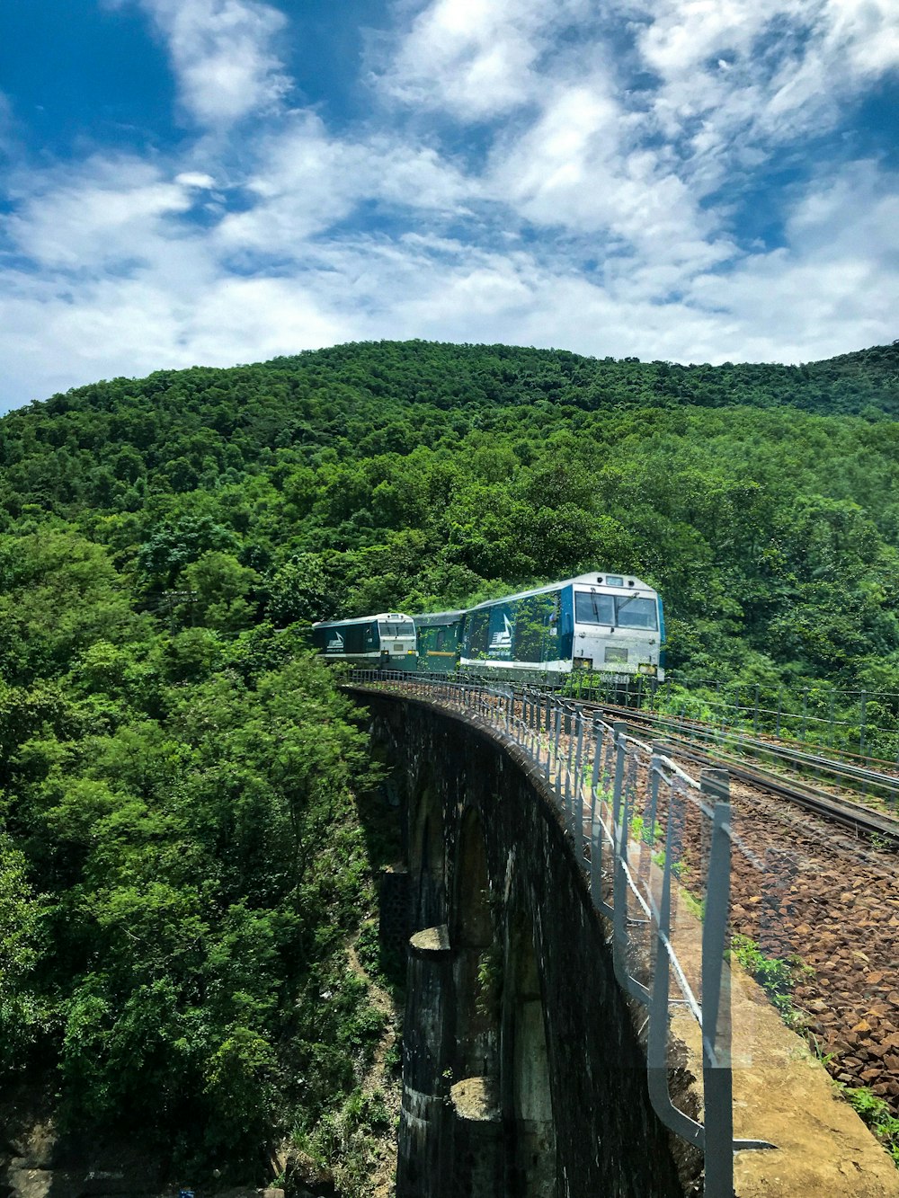 white train on rail near green trees under blue sky and white clouds during daytime