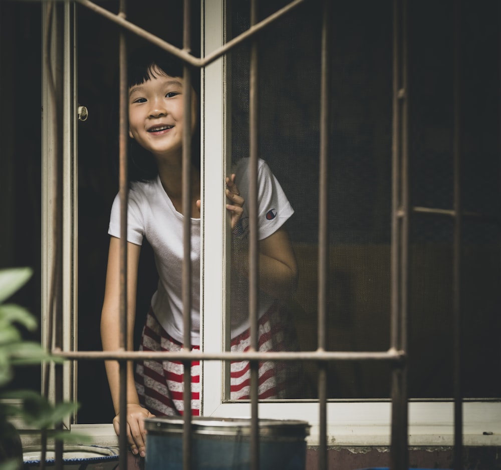 girl in white crew neck t-shirt standing behind black metal gate