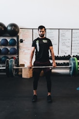 man in black crew neck t-shirt and black shorts carrying barbell