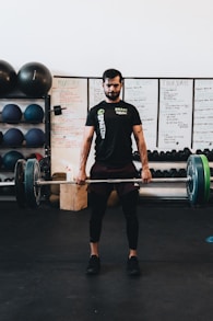 man in black crew neck t-shirt and black shorts carrying barbell