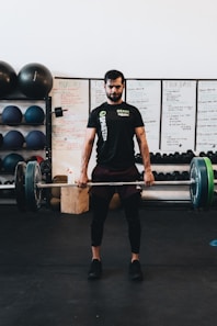 man in black crew neck t-shirt and black shorts carrying barbell