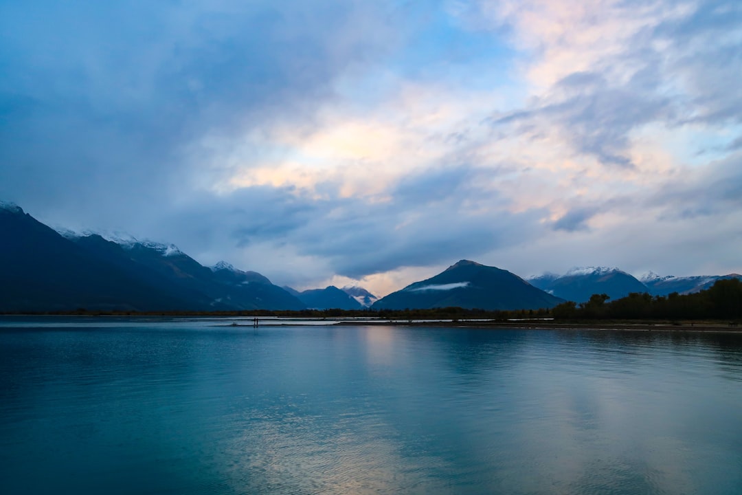 blue body of water near mountain under white clouds and blue sky during daytime