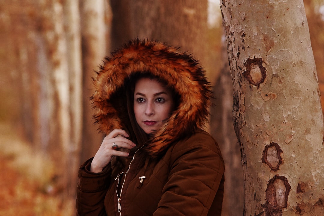 woman in brown fur hoodie standing beside brown tree