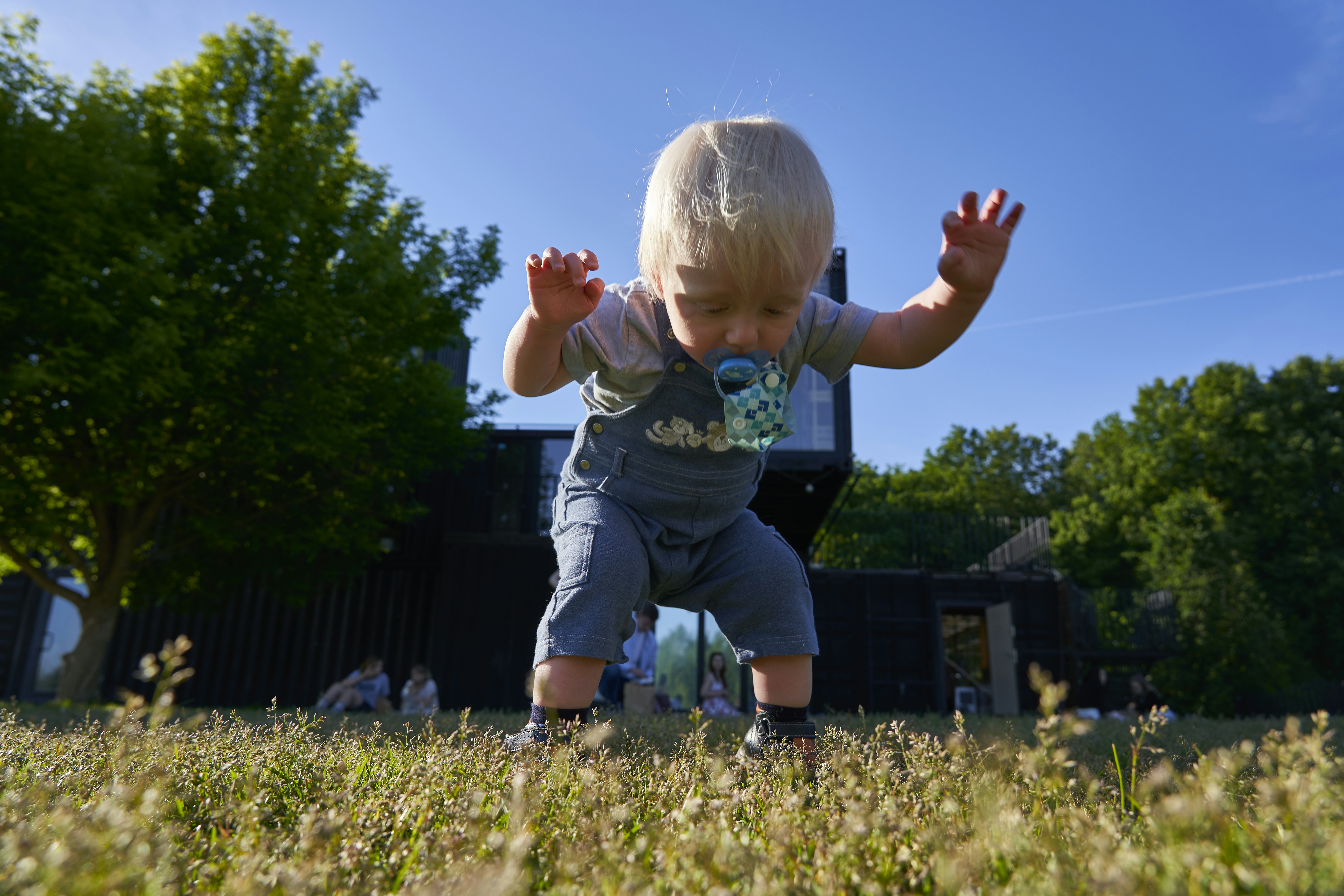 girl in blue denim dungaree pants jumping on green grass field during daytime