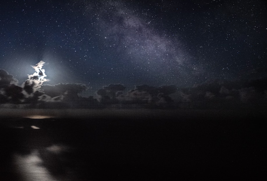 A serene night sky filled with stars and a glowing moon over a tranquil ocean.
