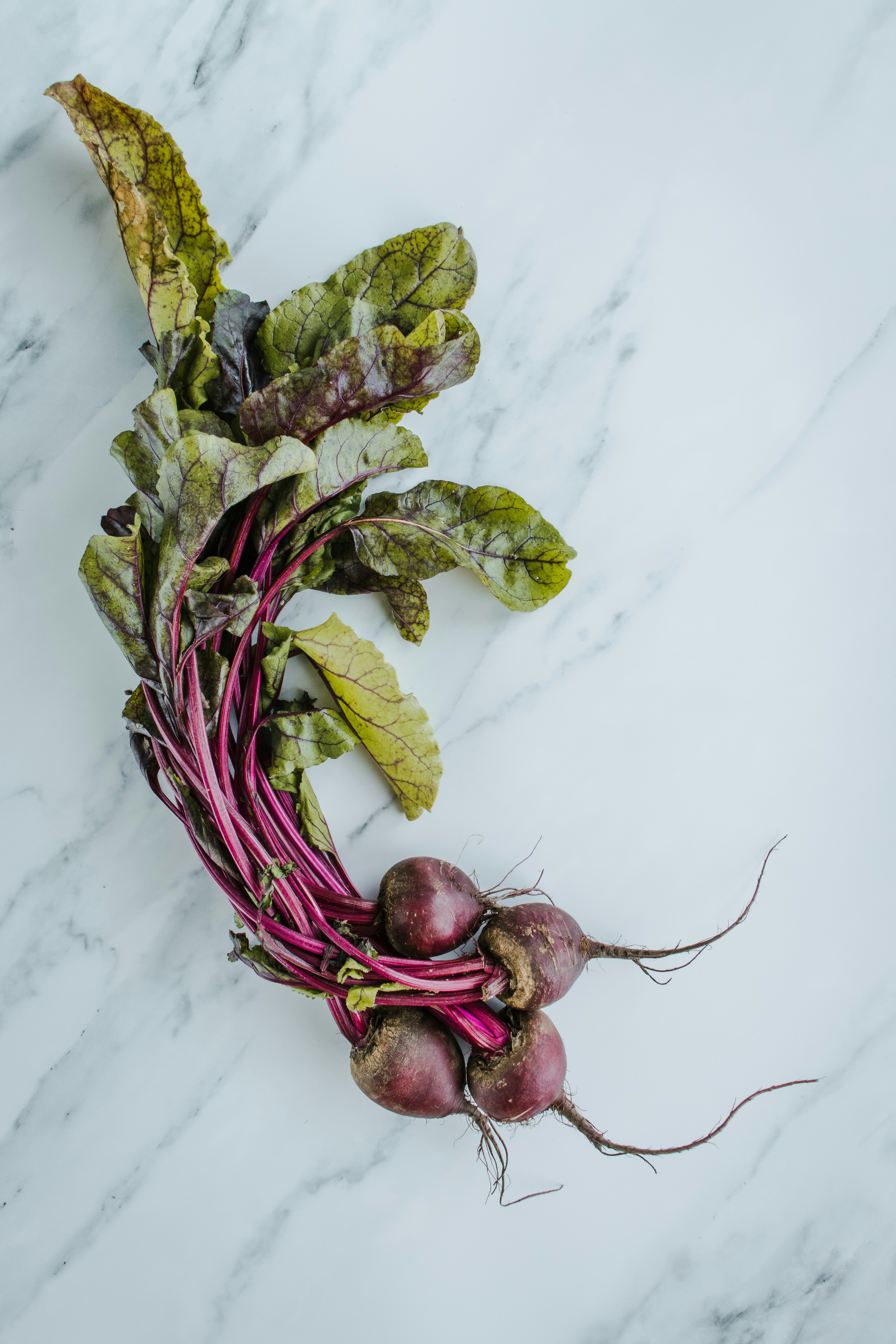 A glass of deep, ruby-red juice with a raw beet, an apple, and a lemon on the side