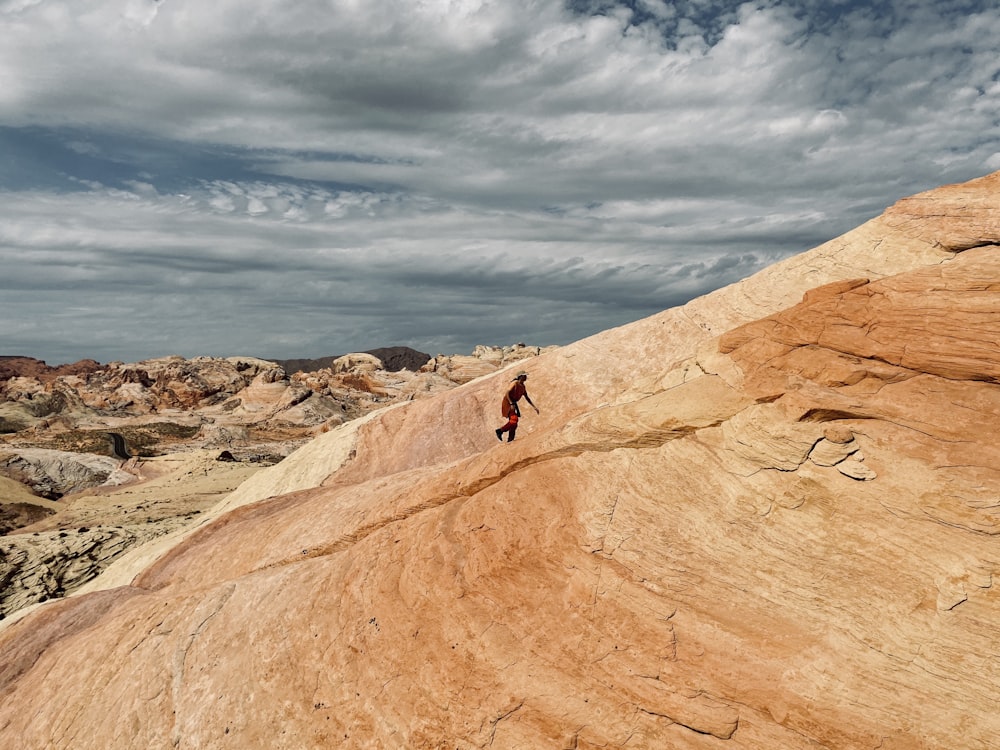 person in black jacket standing on brown rock formation under white clouds during daytime