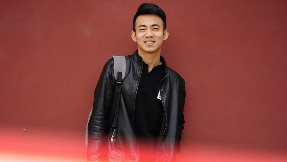 man in black leather jacket standing beside red wall
