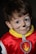 A young child is wearing a red costume with a yellow collar and a badge featuring a flame. The child's face is painted with whiskers and a small black nose, giving them the appearance of a cat or animal character.