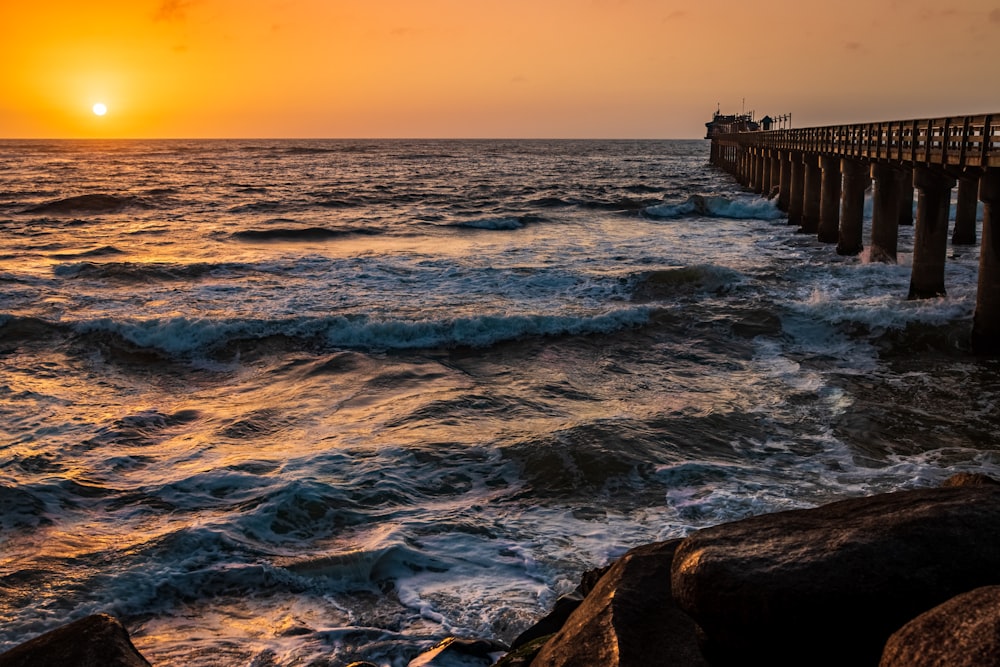 Olas del mar rompiendo en el muelle de madera marrón durante la puesta del sol