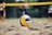 A close-up of a futevôlei ball on the sandy court with players in the background.