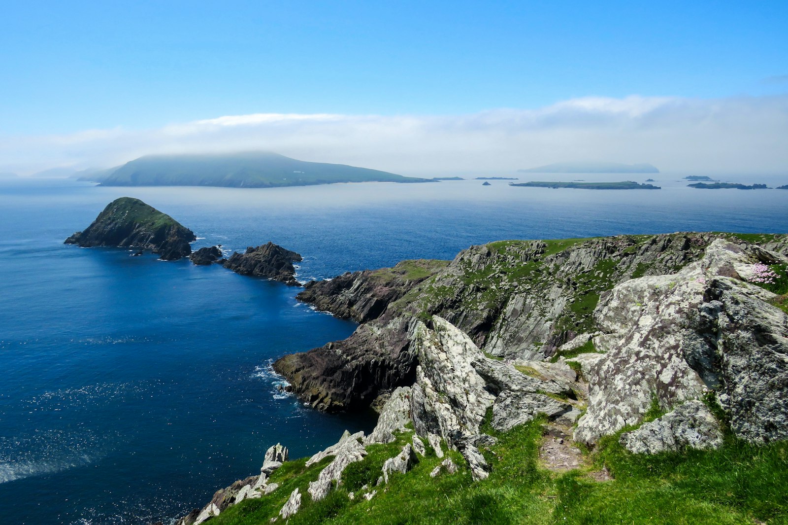 Rocky headland dropping to a blue sea with the humps of offshore islands on the horizon
