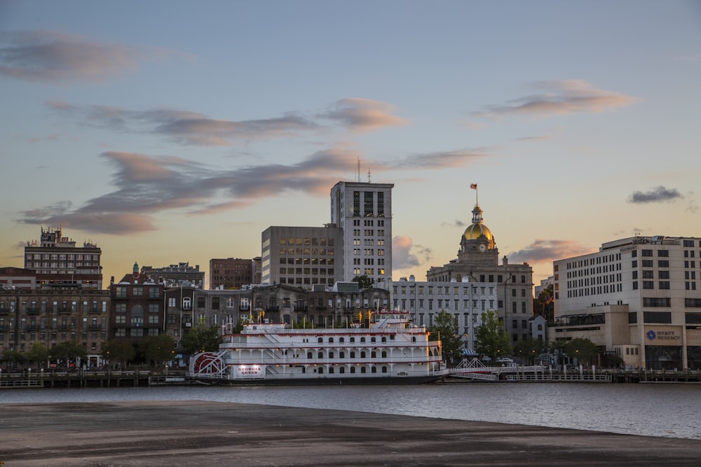 Bateau blanc et brun sur la mer près des bâtiments de la ville au coucher du soleil