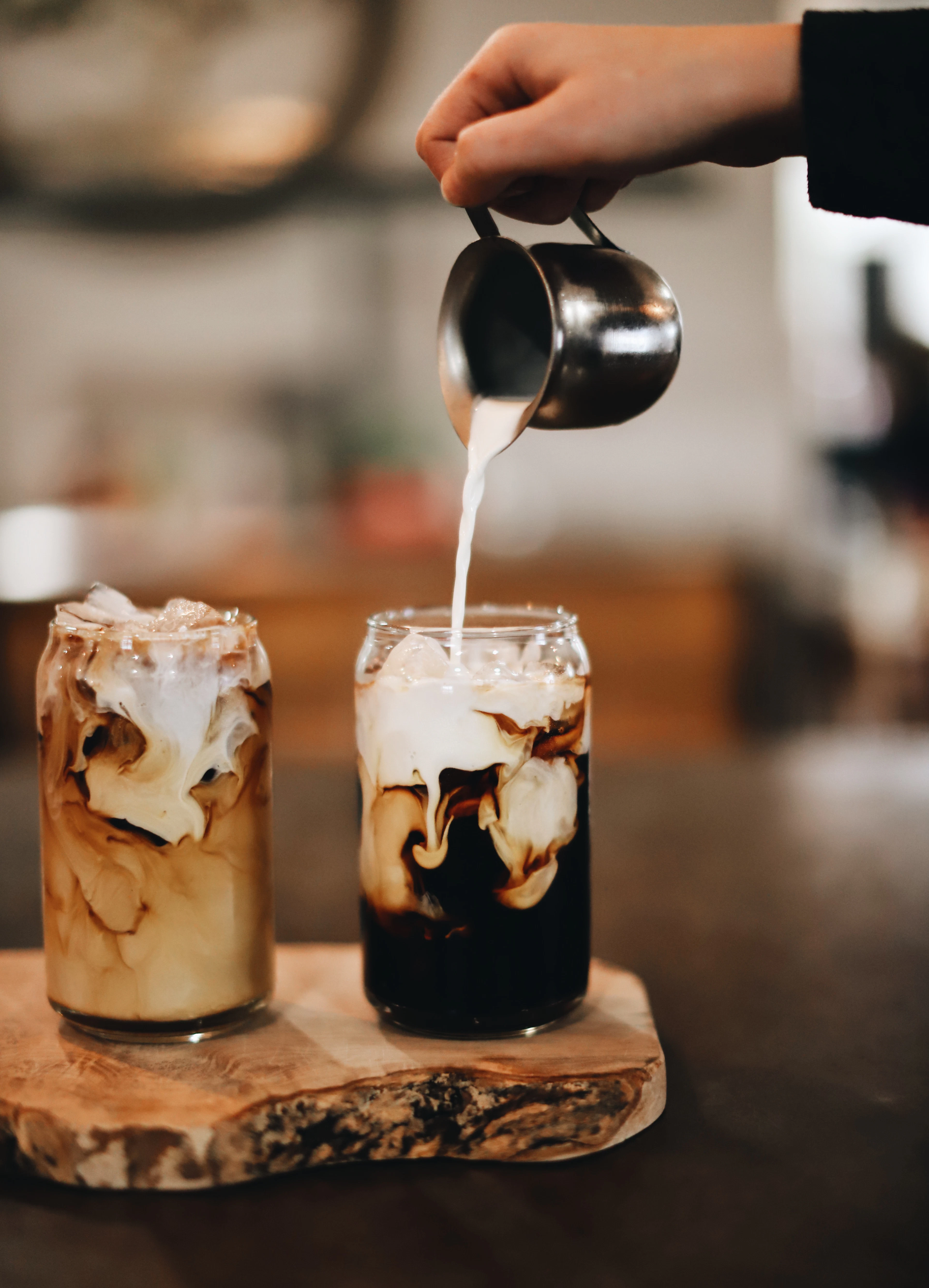 Milk being poured into a tall glass of iced coffee