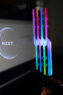 A sleek and modern computer setup features RGB RAM sticks from G.Skill, showcasing vibrant colors including pink, blue, green, and orange. The NZXT logo is also visible, likely on a component or a reflection, suggesting a high-performance gaming or custom PC build.