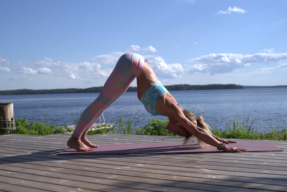 woman in pink shorts and white shirt bending over on brown wooden dock during daytime