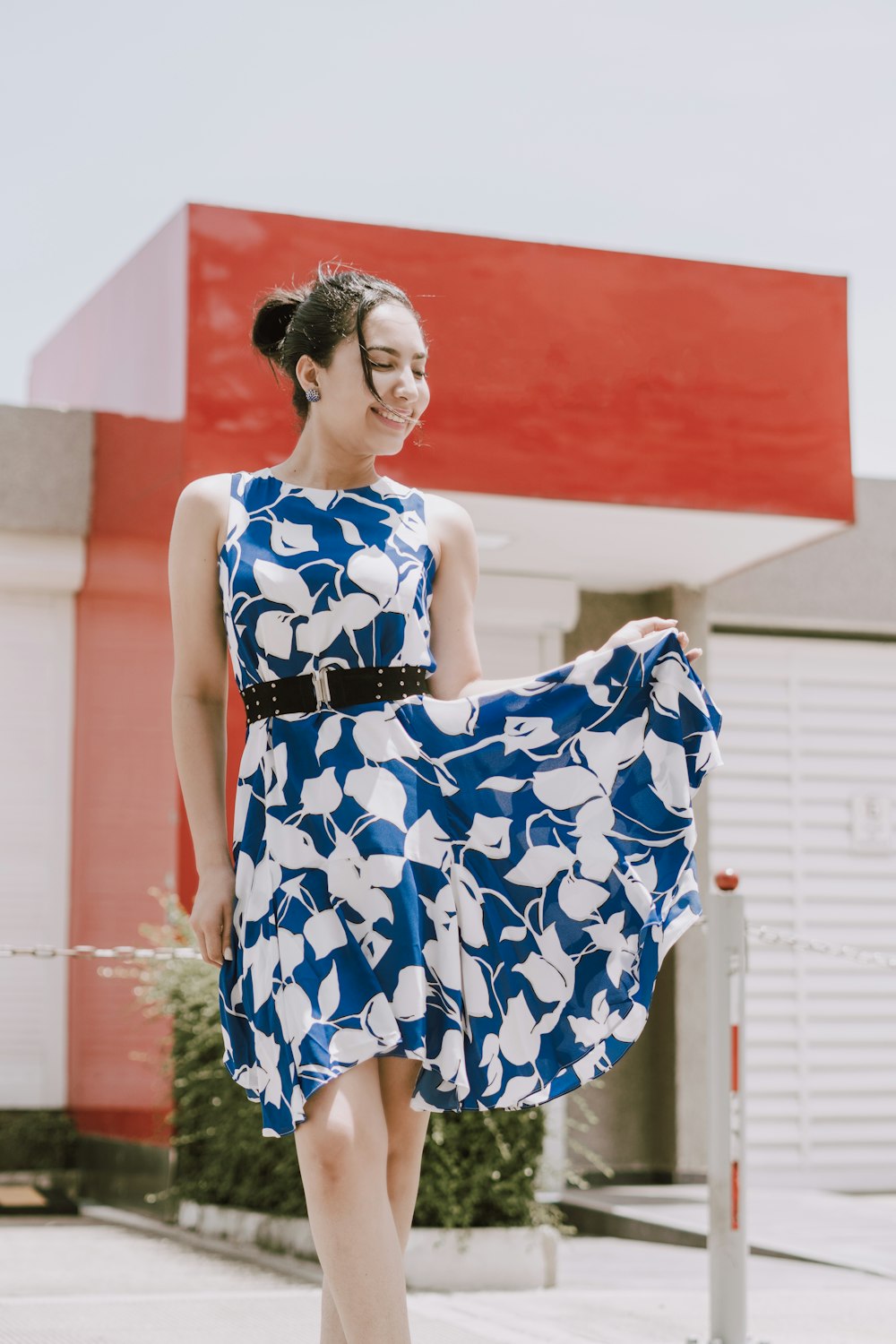 woman in blue and white floral spaghetti strap dress standing near red wall during daytime