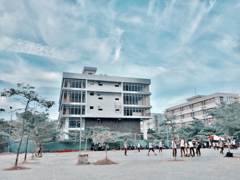A bright campus building of Chenab Medical College with students walking in red and white uniforms under a clear blue sky.