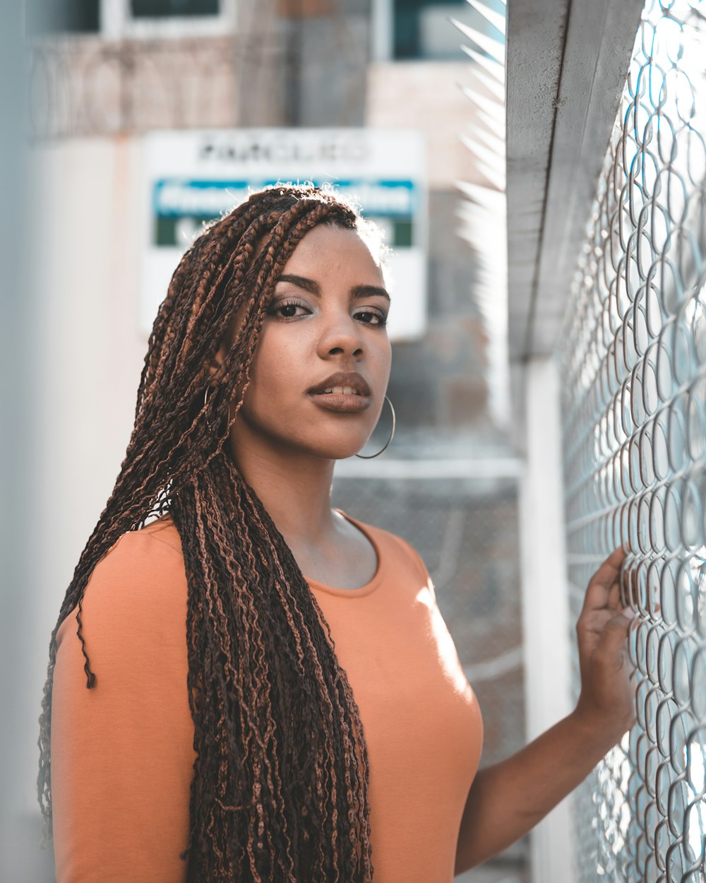 woman in orange tank top standing beside white metal fence during daytime