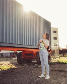 woman in white t-shirt and blue denim jeans standing beside gray roll up door during