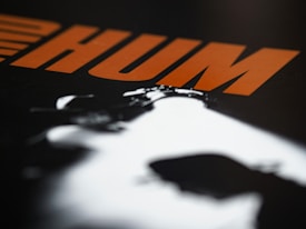 Bold orange letters spell out 'HUM' against a dark background with a high-contrast black and white silhouette in the foreground.
