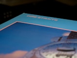 An angled view of an album cover featuring the text 'Dire Straits' in pink, set against a blue and pink background. A partial image of a guitar is visible, emphasizing musical themes.