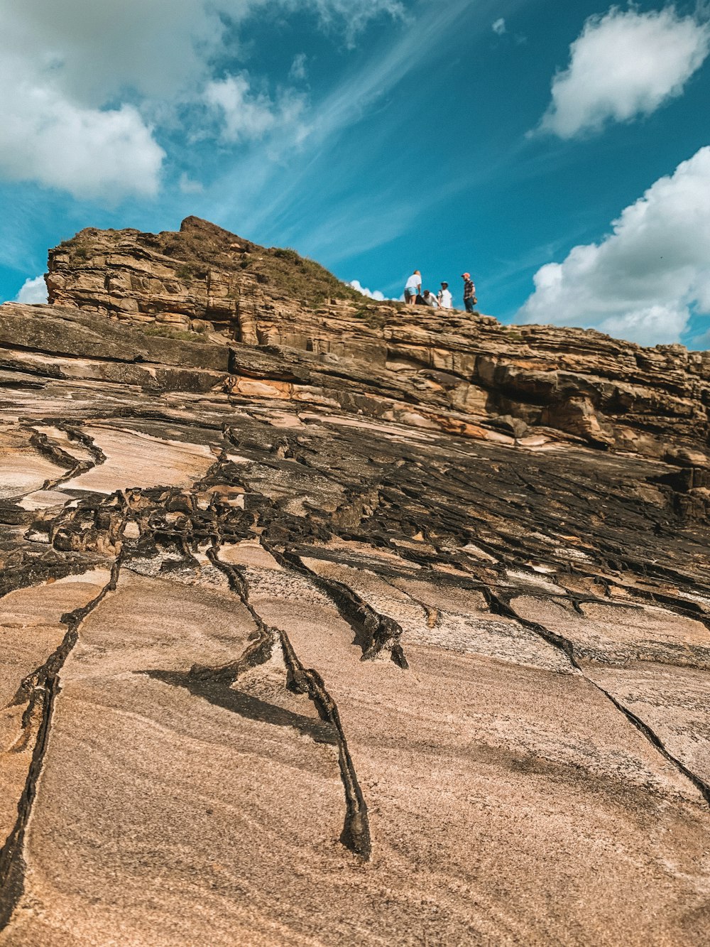 people climbing on brown rocky mountain under blue and white sunny cloudy sky during daytime