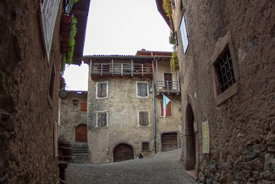 A sunlit cobblestone street in Irsina, Italy, framed by warm stone buildings with subtle Ferrari red accents on shutters and doors.