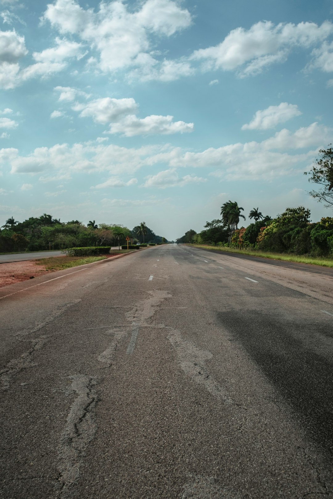 gray asphalt road between green trees under white clouds and blue sky during daytime