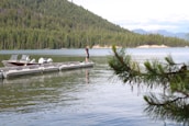 A peaceful lakeside scene with a small boat docked, surrounded by pine trees and clear blue water.