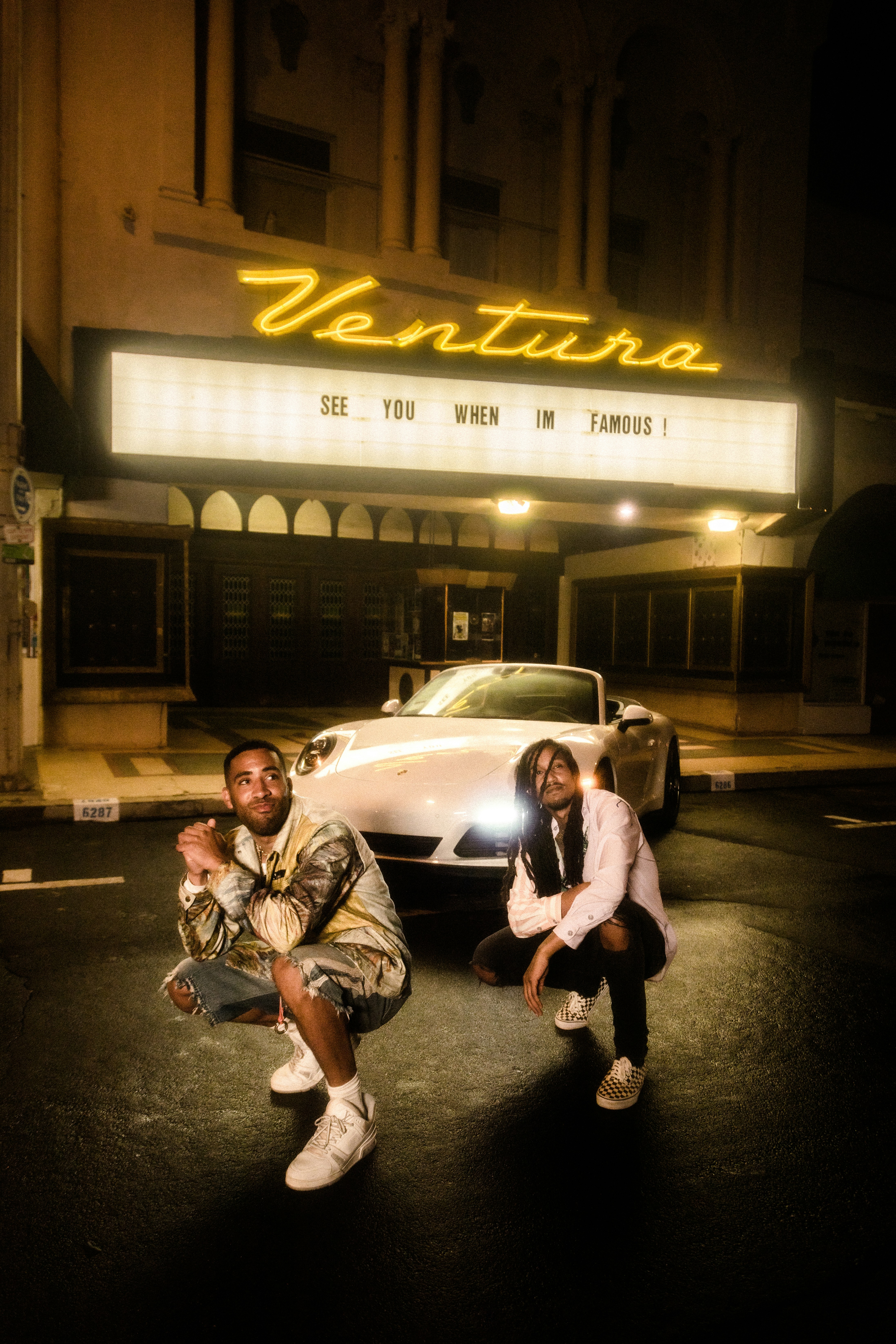 Mann in braun-weiß kariertem Hemd sitzt nachts auf weißer Limousine