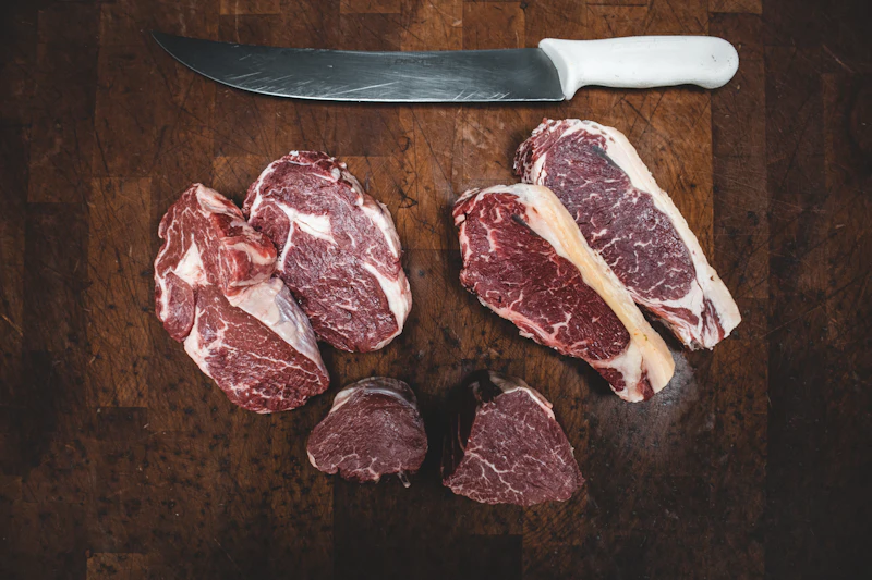 Assorted raw beef cuts beside a butcher's knife on dark wood