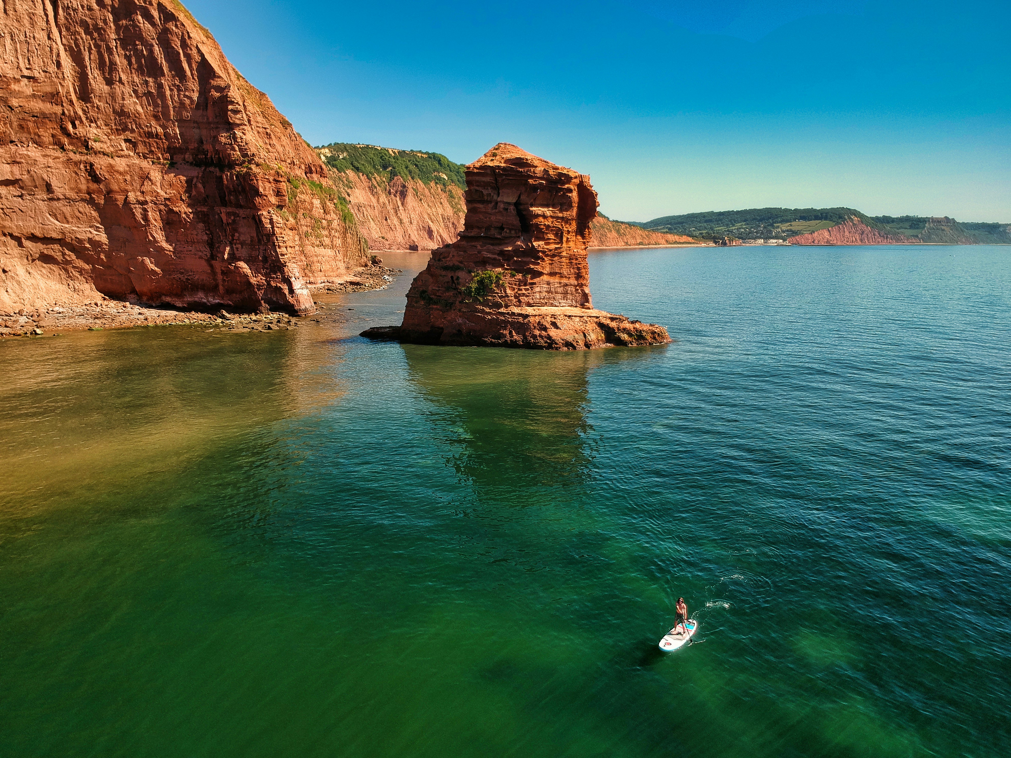 Person standing on rock formation in the sea at sunset along the coastline