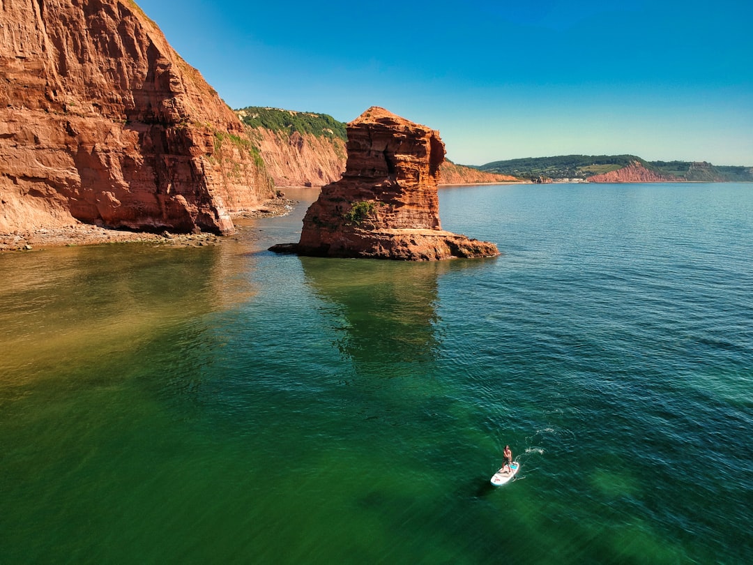 person in white shirt and black shorts standing on rock formation in sea during daytime