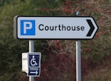 A signpost pointing towards a courthouse parking area. The main sign features a large letter 'P' indicating parking, with the word 'Courthouse' and an arrow pointing right. Below it, there is a smaller sign for accessible parking with a wheelchair symbol.