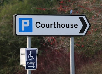 A signpost pointing towards a courthouse parking area. The main sign features a large letter 'P' indicating parking, with the word 'Courthouse' and an arrow pointing right. Below it, there is a smaller sign for accessible parking with a wheelchair symbol.