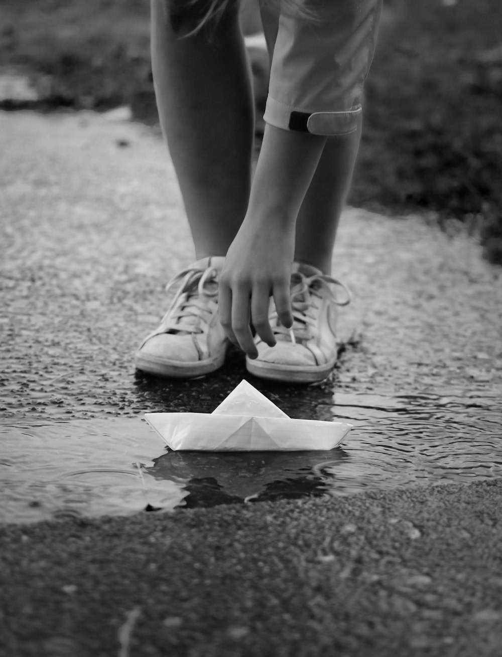 grayscale photo of person in white shorts and sneakers standing on wet road