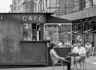 grayscale photo of people sitting on chair in front of table