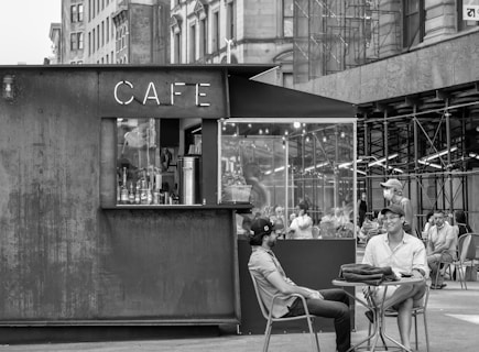 grayscale photo of people sitting on chair in front of table