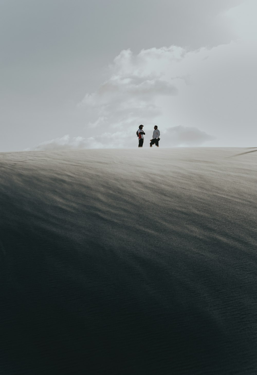 2 person walking on brown sand under white clouds during daytime