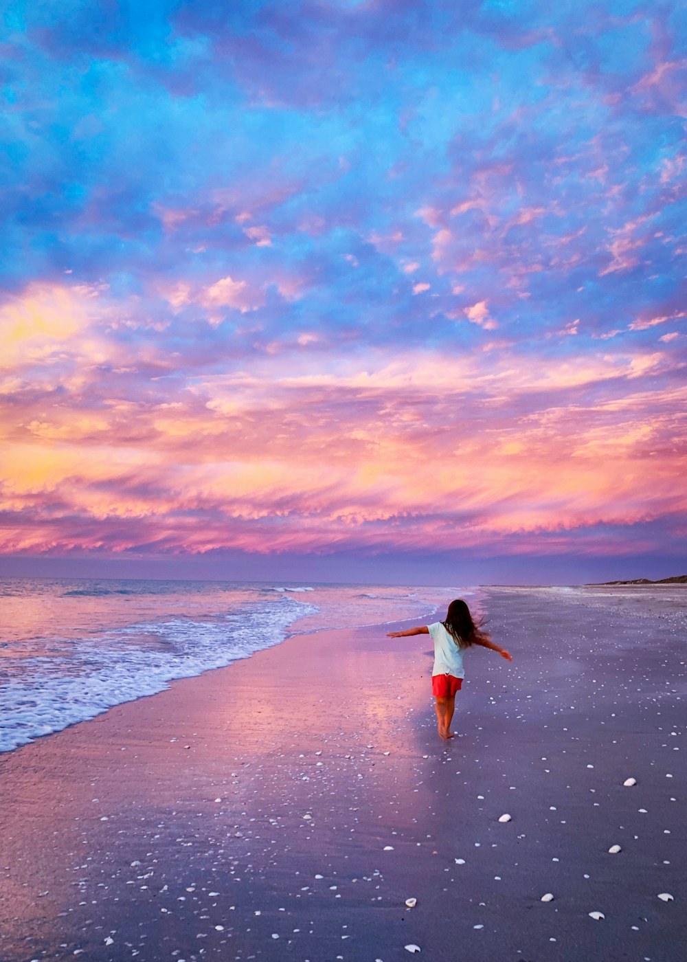 Frau im weißen Kleid geht bei Sonnenuntergang am Strand spazieren