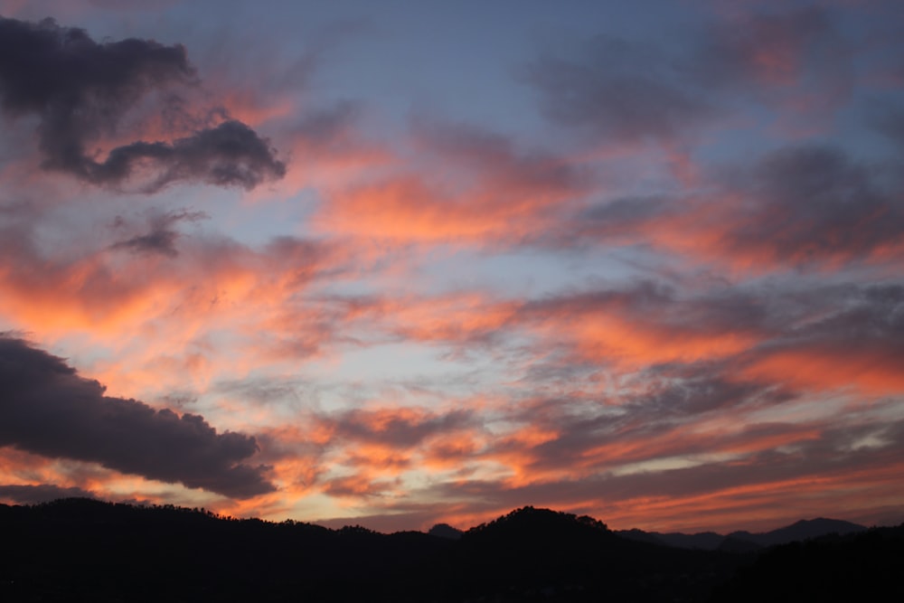 silhouette of mountain under orange and gray clouds