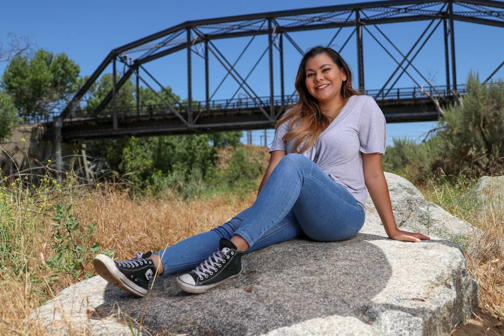 woman in gray shirt and blue denim jeans sitting on gray rock