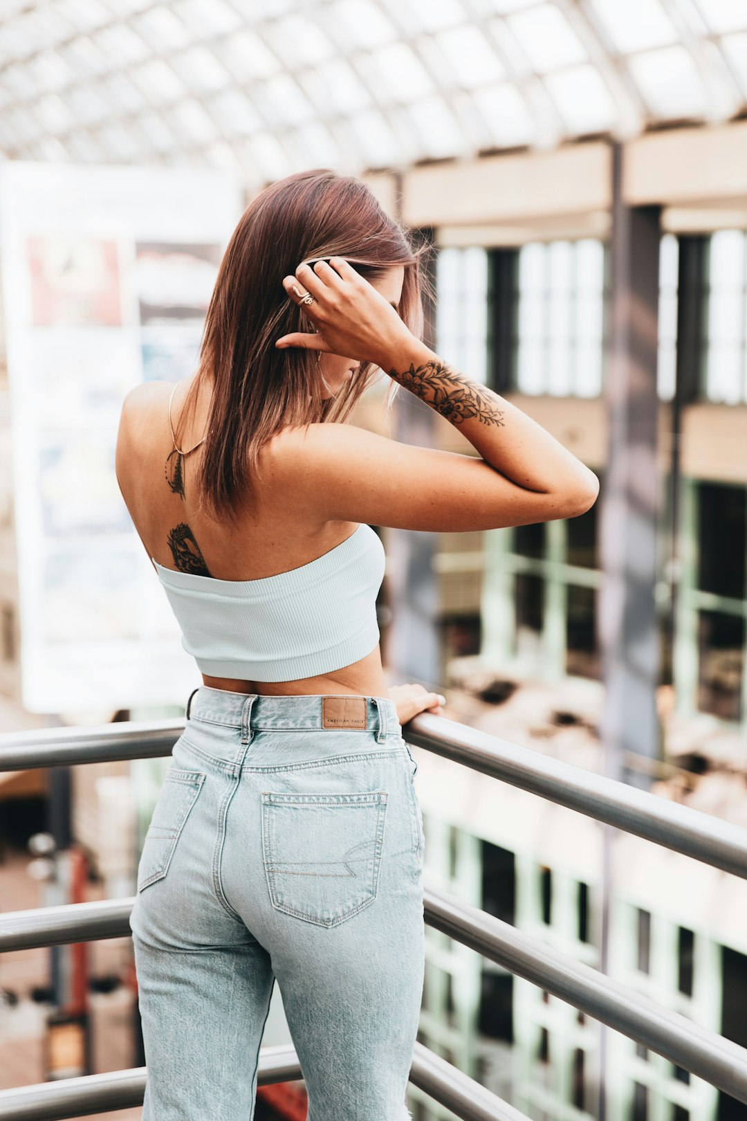 woman in white crop top and blue denim jeans standing near glass window during daytime