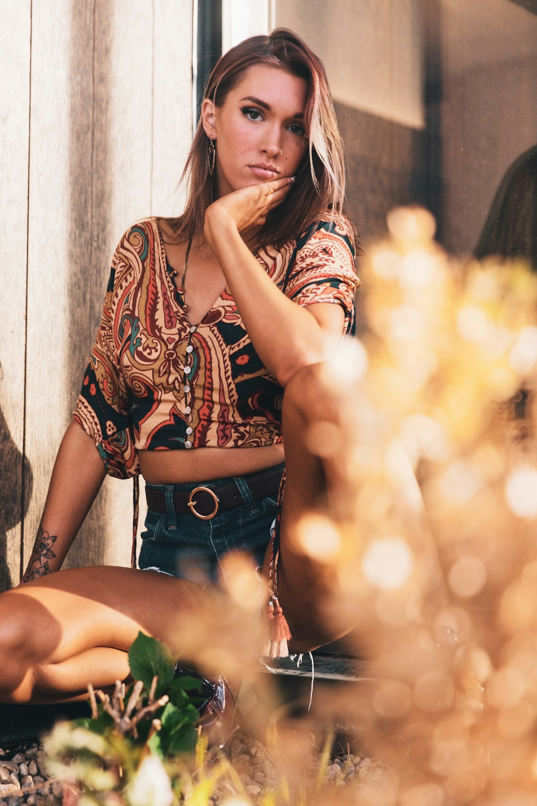 woman in red and white floral shirt and blue denim daisy dukes sitting on brown wooden