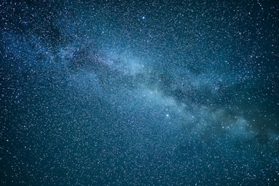 A dense cluster of stars and cosmic dust forming a segment of the Milky Way galaxy stretches diagonally across a dark night sky. Countless stars with varying brightness are scattered throughout the image.