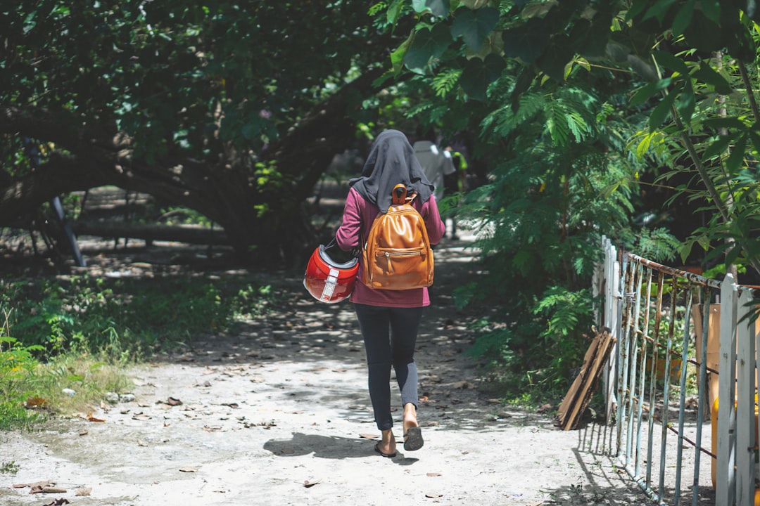 woman in black jacket and red backpack walking on dirt road during daytime