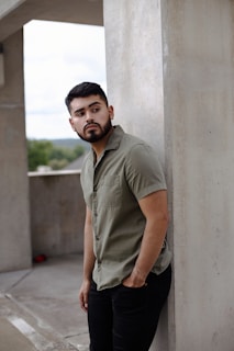 man in gray button up shirt and black pants standing beside white concrete wall during daytime