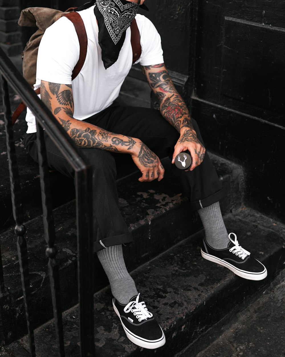 Hombre con pantalones negros y zapatillas Nike negras sentado en barandillas de metal negro